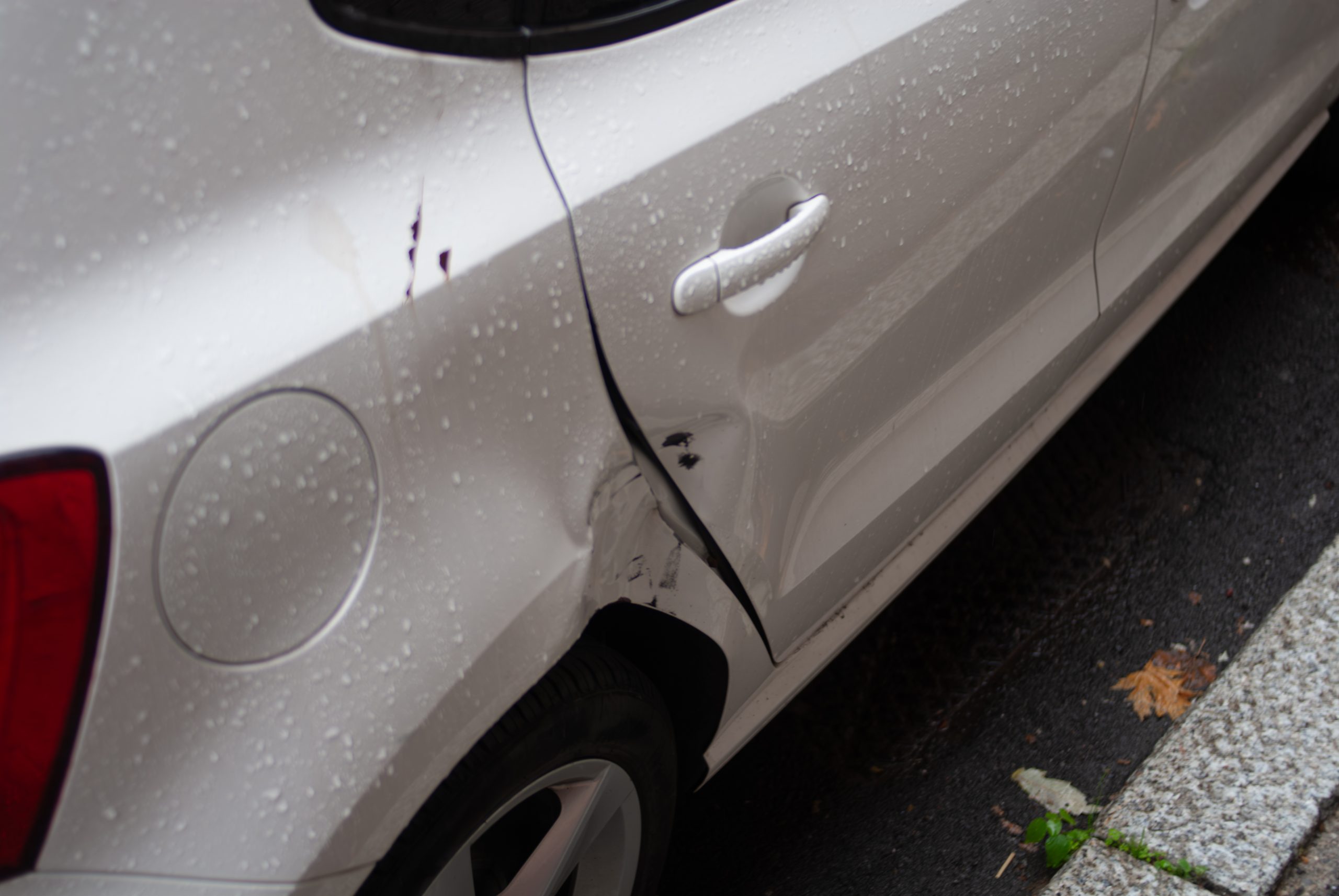 99910224-white-car-with-heavy-rear-quarter-and-door-damage-from-a-side-impact-closeup-of-dented-scratched-bodywork-and-paint-loss